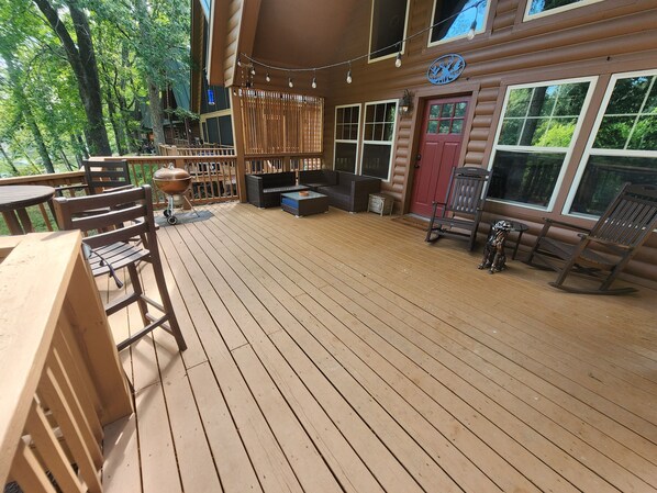 Una terraza de madera con mobiliario exterior, una parrilla y una puerta roja.