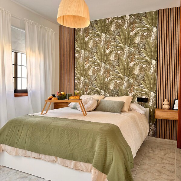 A bedroom with a bed, a bedside table, a lamp, and a window with curtains.