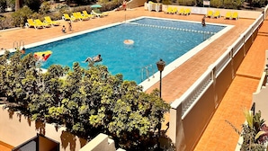 A swimming pool with sun loungers and a building with balconies in the background.