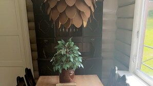 Une table à manger en bois, avec des chaises, une plante en pot et un élément décoratif suspendu, dans une pièce dotée d’une fenêtre et d’une porte.
