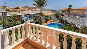 A balcony with a pool, surrounded by lush greenery and a clear view of the sea.
