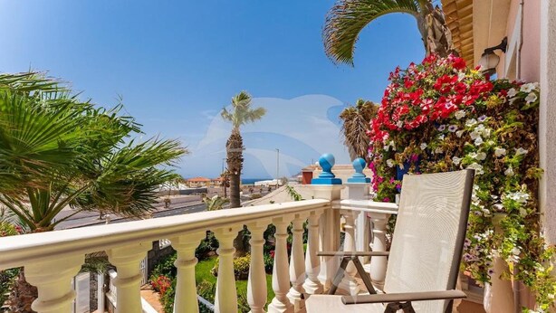 A balcony with a white balustrade, a chair, and a flower wall.