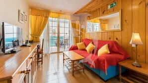 A room with a wooden interior, a sofa with yellow cushions, a table, a TV, and a mirror on the wall. - Relax in El Médano's Modern Sea View Apartment (Granadilla de Abona)