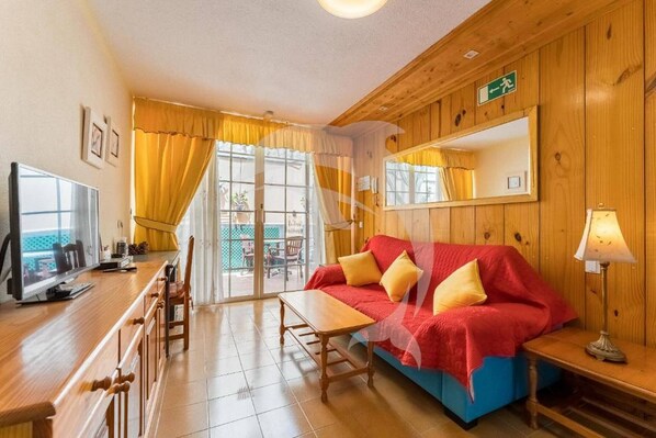 A room with a wooden interior, a sofa with yellow cushions, a table, a TV, and a mirror on the wall. - Relax in El Médano's Modern Sea View Apartment (Granadilla de Abona)