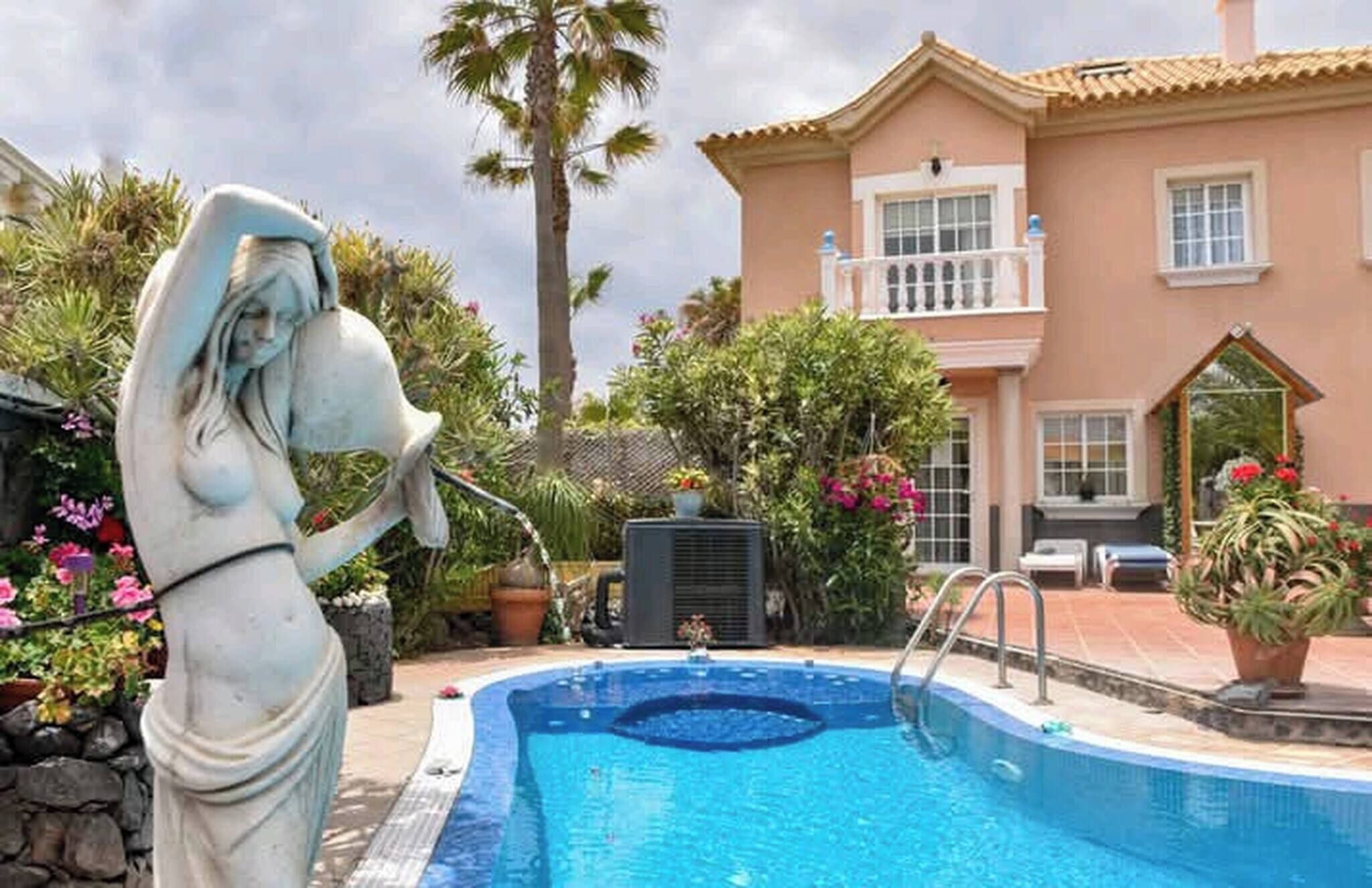 Une piscine ornée d’une statue, une maison dotée d’un balcon et diverses plantes.