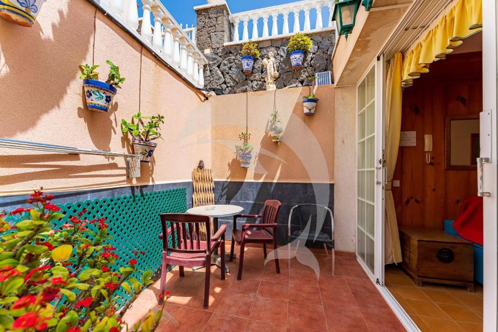 A small patio with a table and chairs, potted plants, and a stone wall.