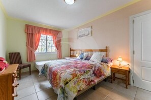 A bedroom with a bed, a chair, a bedside table with a lamp, a window with curtains, and a door. - Relax in El Médano's Modern Sea View Apartment (Granadilla de Abona)