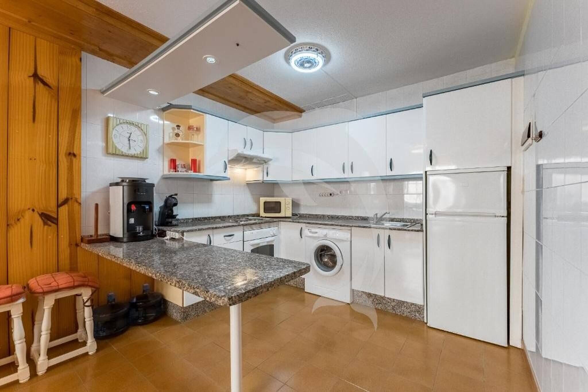 A compact kitchen with white cabinets, a granite countertop, a washing machine, and a refrigerator.