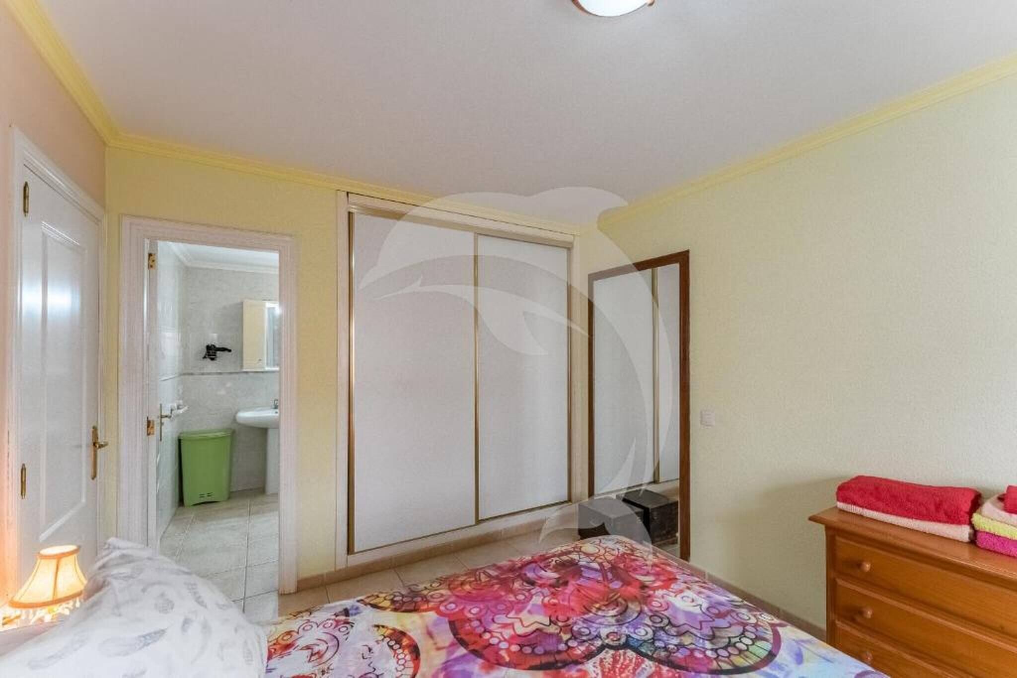 A bedroom with a bed, a dresser, a mirror, and a door leading to a bathroom.