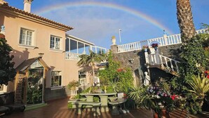 A two-story building with a balcony, surrounded by lush greenery and a palm tree. - Relax in El Médano's Modern Sea View Apartment (Granadilla de Abona)