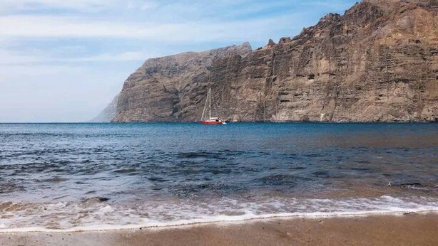 A coastal scene with a rocky cliff and a boat in the water. - Relax in El Médano's Modern Sea View Apartment (Granadilla de Abona)
