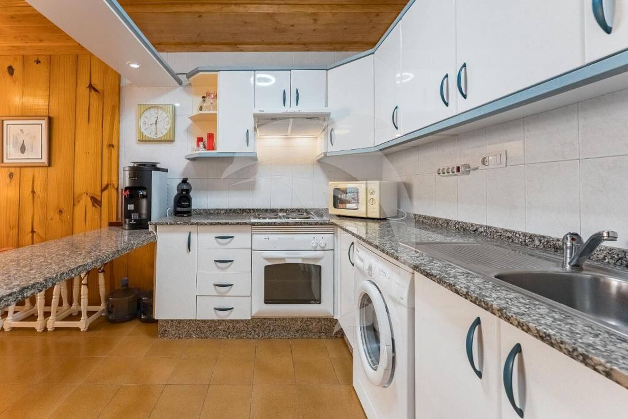 A compact kitchen with white cabinets, a granite countertop, a built-in oven, a washing machine, and a sink.