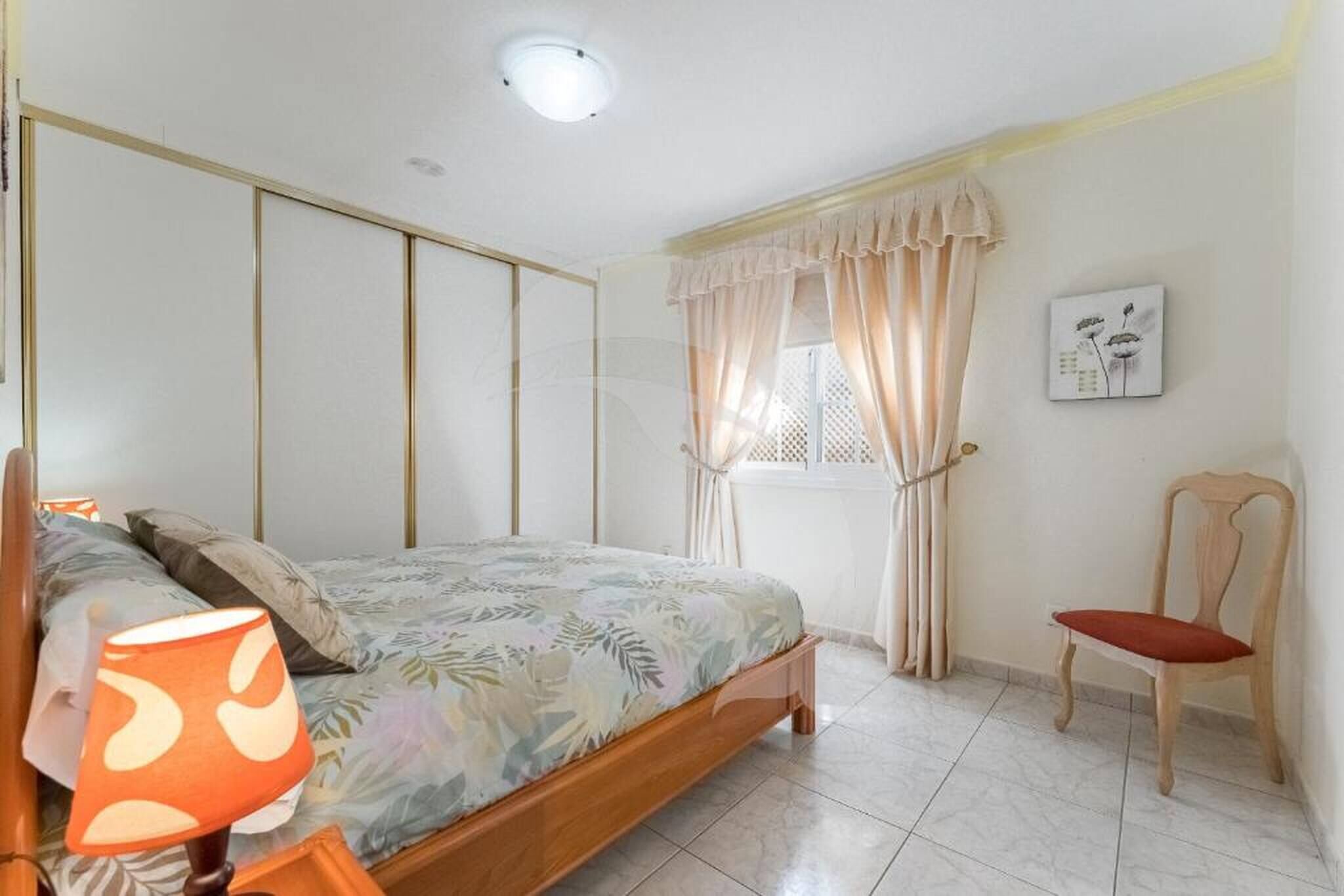 A bedroom with a bed, a chair, a lamp, and a window with curtains.