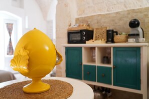 A yellow decorative object on a table with a woven placemat, a teal cabinet with drawers, and a microwave above it. - Maison Blanc - Iconic Stone Architecture (Ostuni)