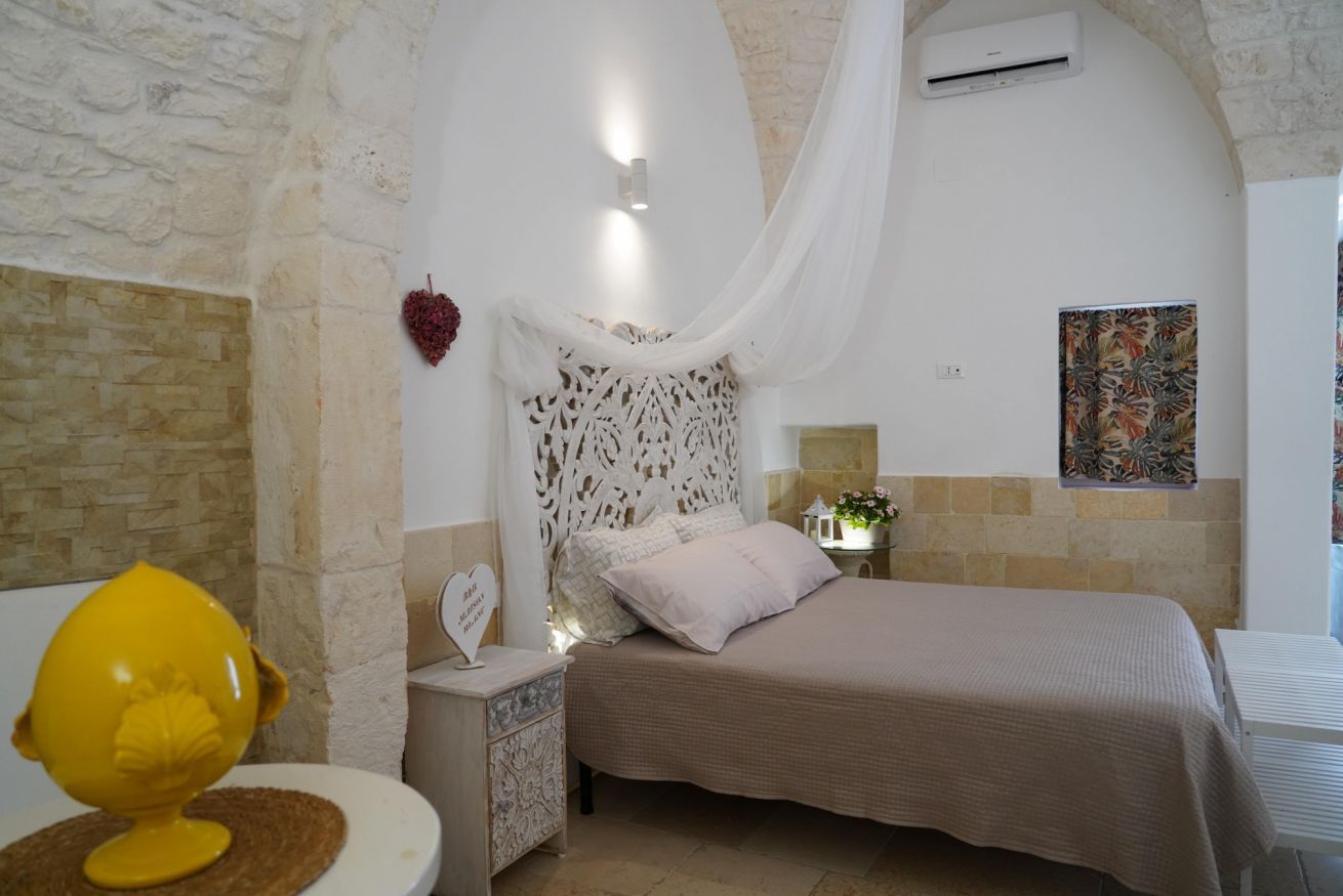 A bedroom with a stone wall, a bed with a white canopy, a bedside table with a decorative item, and a wall-mounted air conditioner.