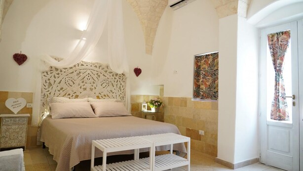 A bedroom with a bed, a bedside table, a decorative headboard, and a wall-mounted air conditioning unit.