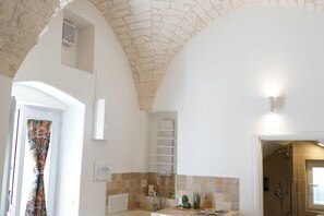 Une salle de bain avec une douche, un lavabo et une petite étagère contenant des articles de toilette. On y trouve également un porte-serviettes et une fenêtre avec un rideau.