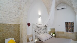 A bedroom with a stone wall, a bed with a white canopy, a nightstand with a heart-shaped sign, and a wall-mounted air conditioner.