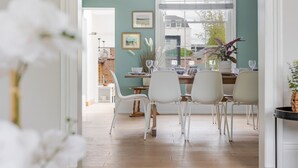 Een eetgedeelte met witte stoelen, een houten tafel en een raam met luiken.
