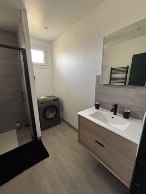 A modern bathroom with a built-in washing machine, a sink with two faucets, and a large mirror above the vanity.
