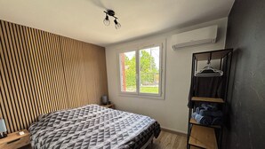 A bedroom with a bed, a wooden slat wall, a window, a hanging rack with towels, and a ceiling light fixture. - Nature & jacuzzi, near Sancerre, Guedelon, Lac de Bourdon, St Fargeau, Pouilly (Cosne-Cours-sur-Loire)