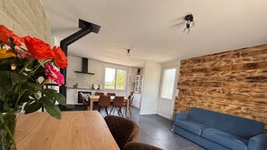 A modern living room with a wooden dining table, a blue sofa, and a wooden accent wall. - Nature & jacuzzi, near Sancerre, Guedelon, Lac de Bourdon, St Fargeau, Pouilly (Cosne-Cours-sur-Loire)