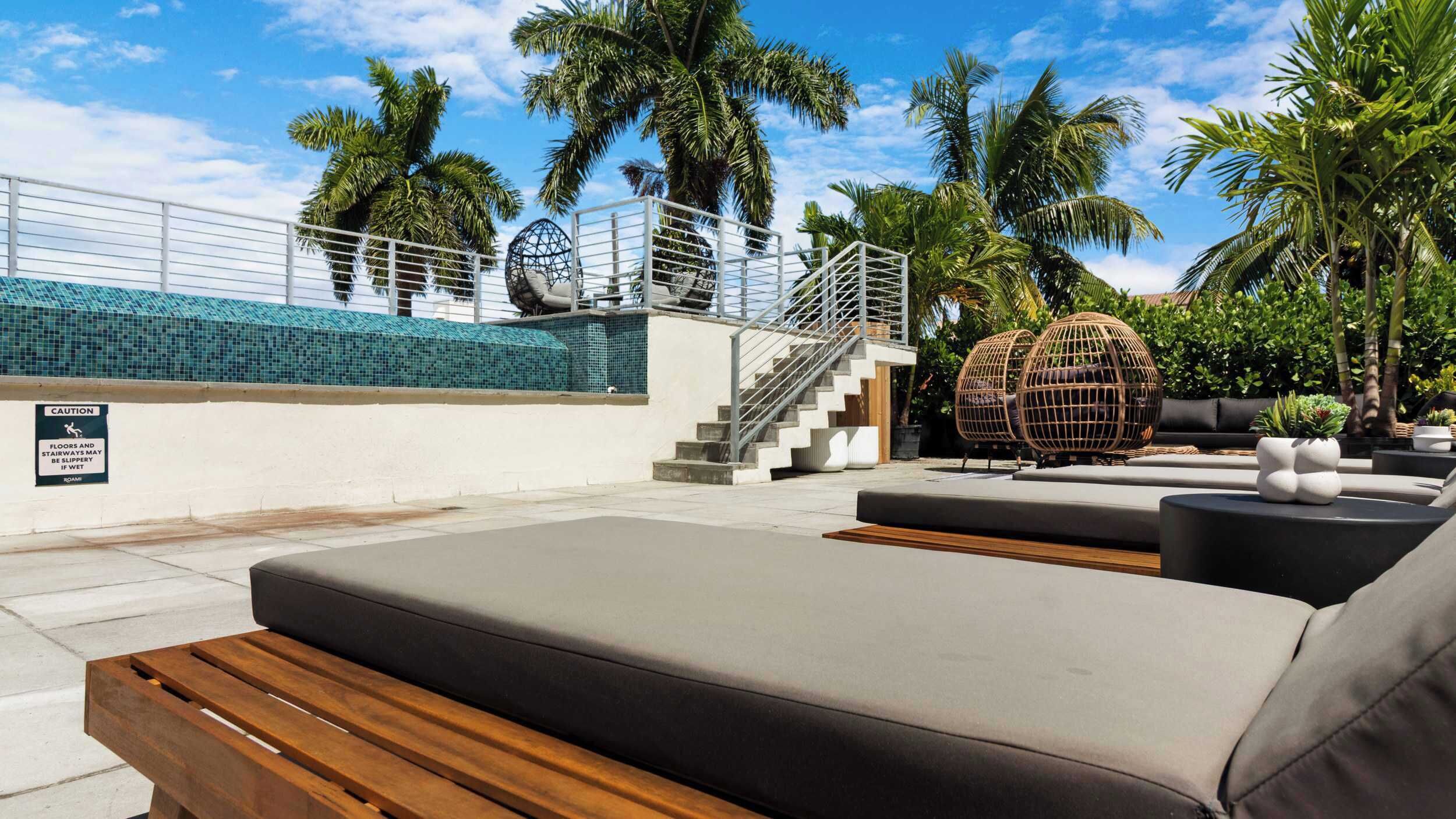 A poolside area with lounge chairs, a staircase, and palm trees.