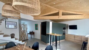 A modern kitchen with dark green cabinets, a wooden dining table with chairs, and a hanging wicker chandelier. - Villa blanche de Ré (rivedoux)