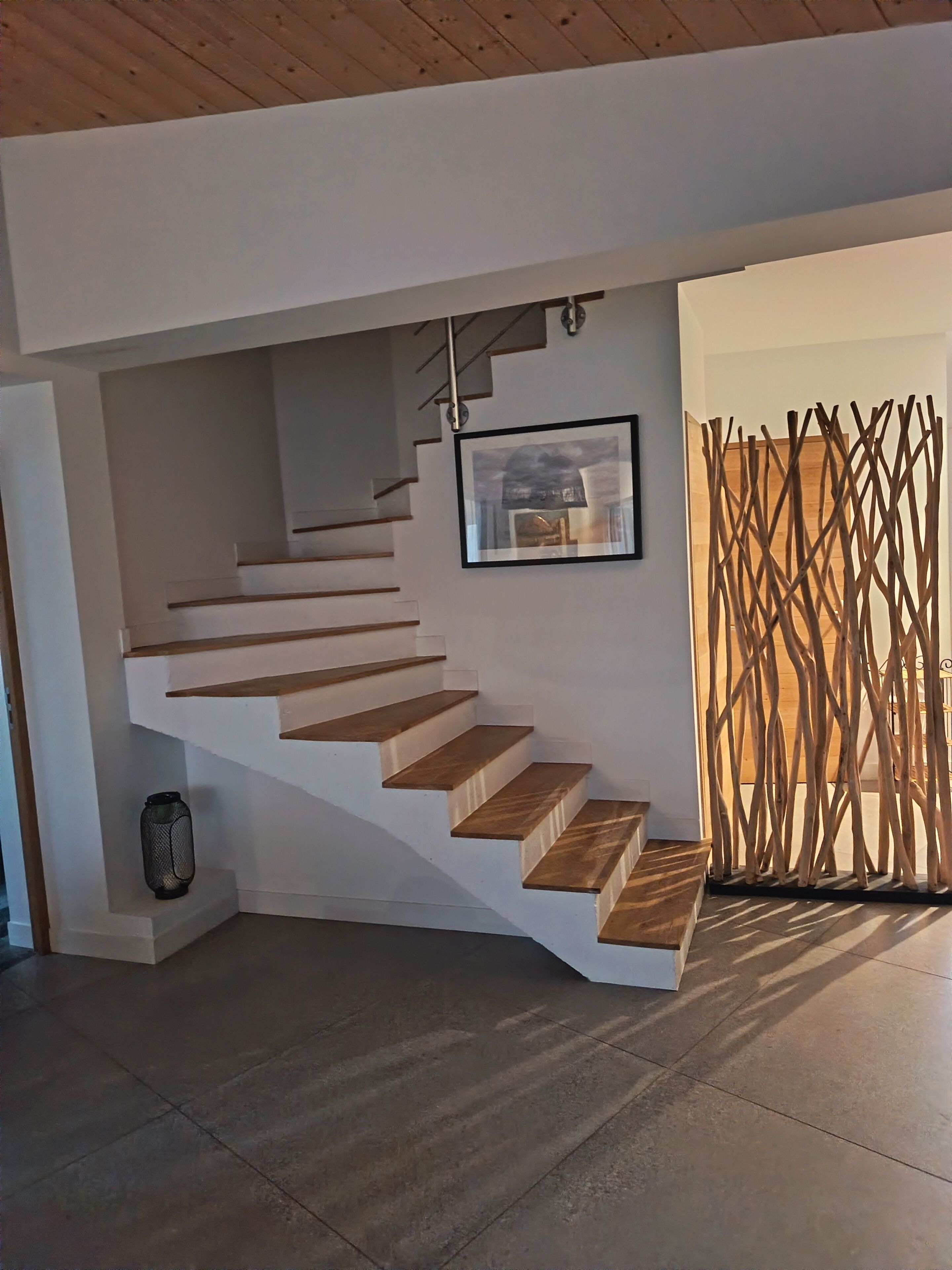 A modern staircase with wooden steps and a metal railing, leading to a landing area with a framed artwork.