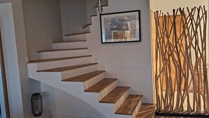 A modern staircase with wooden steps and a metal railing, leading to a landing area with a framed artwork. - Villa blanche de Ré (rivedoux)
