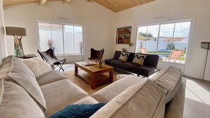 A spacious living room with a high wooden ceiling, large windows, a sofa set, a coffee table, and a painting on the wall. - Villa blanche de Ré (rivedoux)