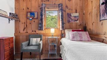Una habitación acogedora con una cama, una silla, una mesita, una lámpara y una ventana con cortinas.