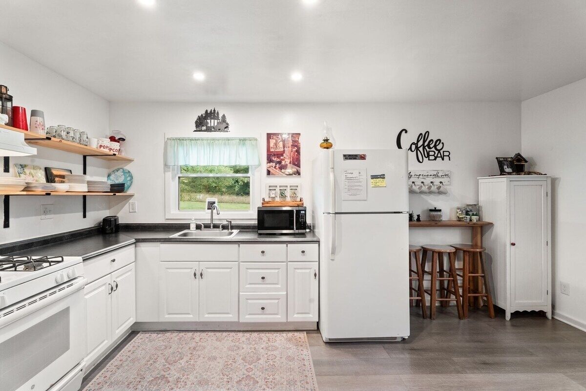 A modern kitchen with white cabinetry, a gas stove, a microwave, and a refrigerator. There is a window with a view of greenery outside.