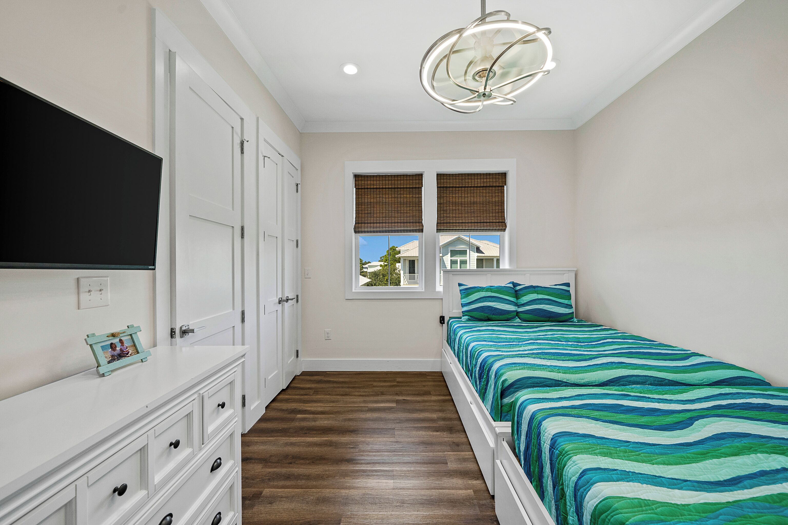 A bedroom with a bed, dresser, TV, and a window with blinds.