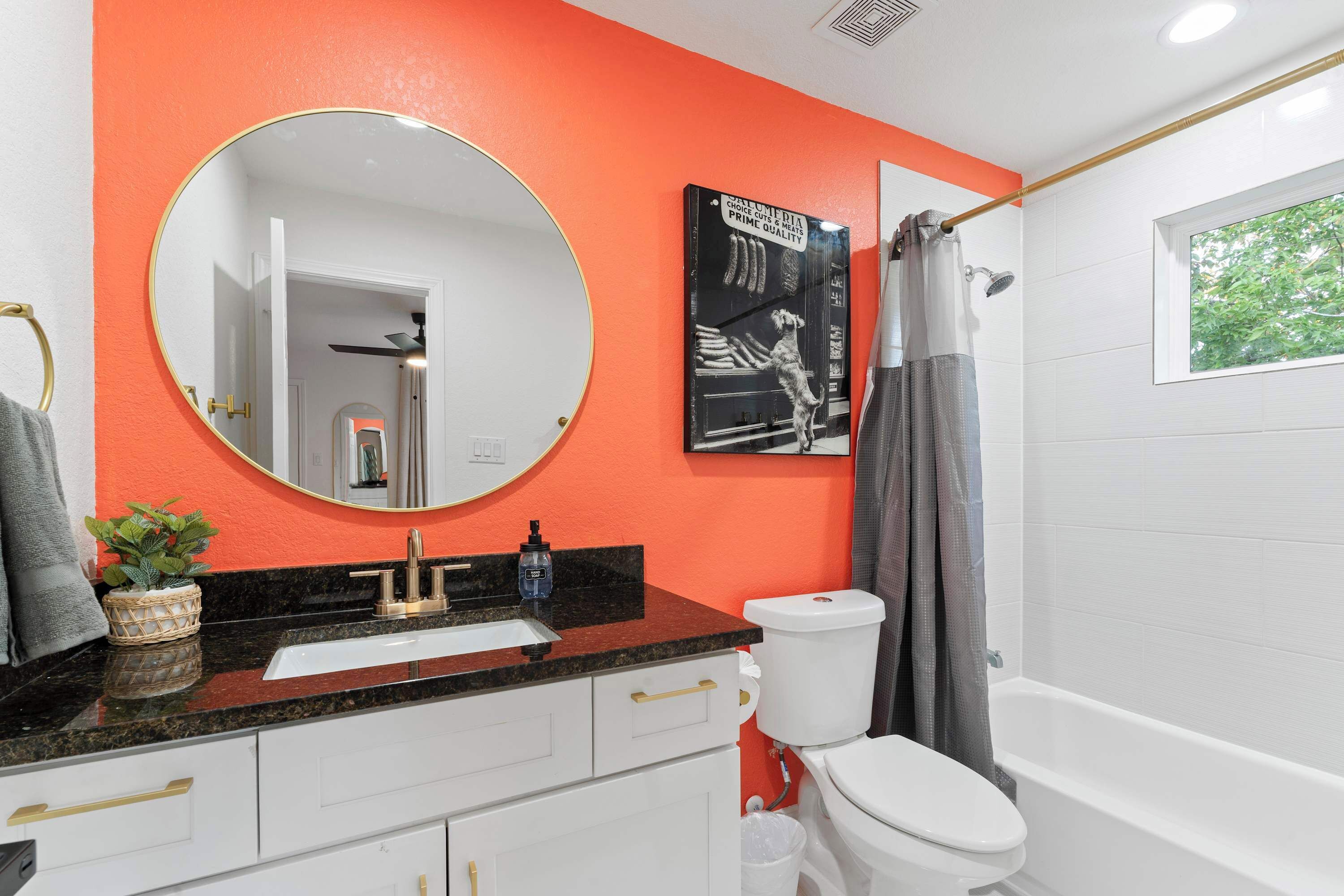 A bathroom with a white toilet, a black sink with gold handles, a round mirror, and a shower curtain.
