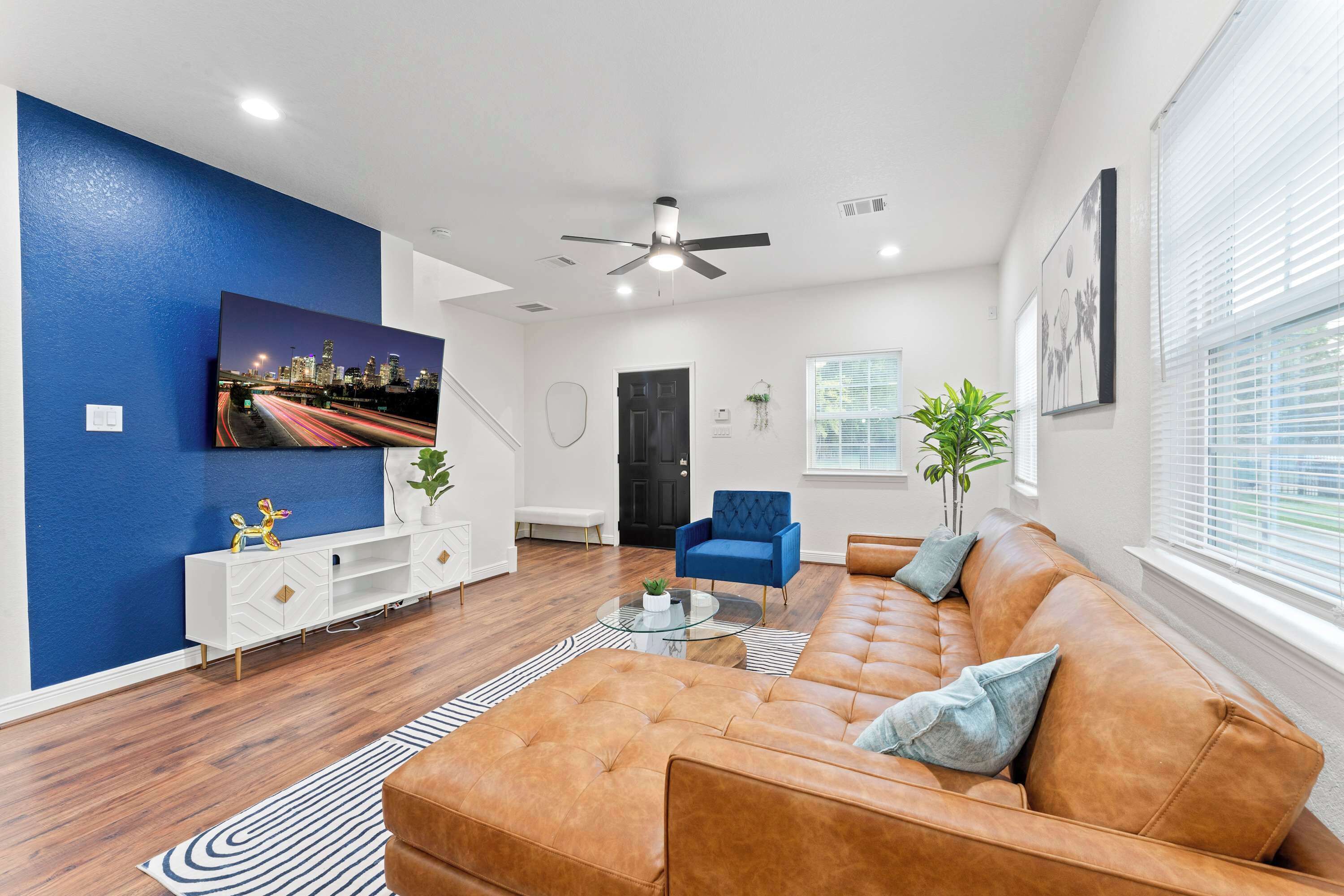Ein modernes Wohnzimmer mit einem braunen Ledersofa, einem blauen Sessel, einer weißen Unterhaltungsecke und einem Stadtbild an der Wand.
