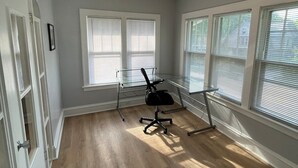 Una habitación con piso de madera, una silla de oficina negra, un escritorio con cubierta de vidrio y una lámpara en el techo.