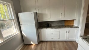 Una cocina con armarios blancos, un refrigerador blanco y una encimera de madera.