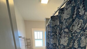 Un baño con inodoro, ventana y cortina de ducha estampada con motivos florales.
