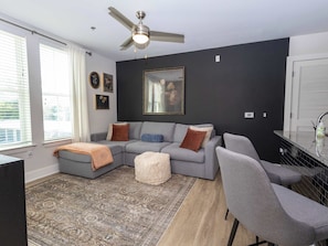 A living room with a gray sectional sofa, a white ottoman, a gray armchair, a ceiling fan, and a large mirror on the wall.