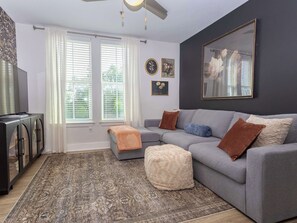 A living room with a grey sofa, ottoman, and a patterned rug.