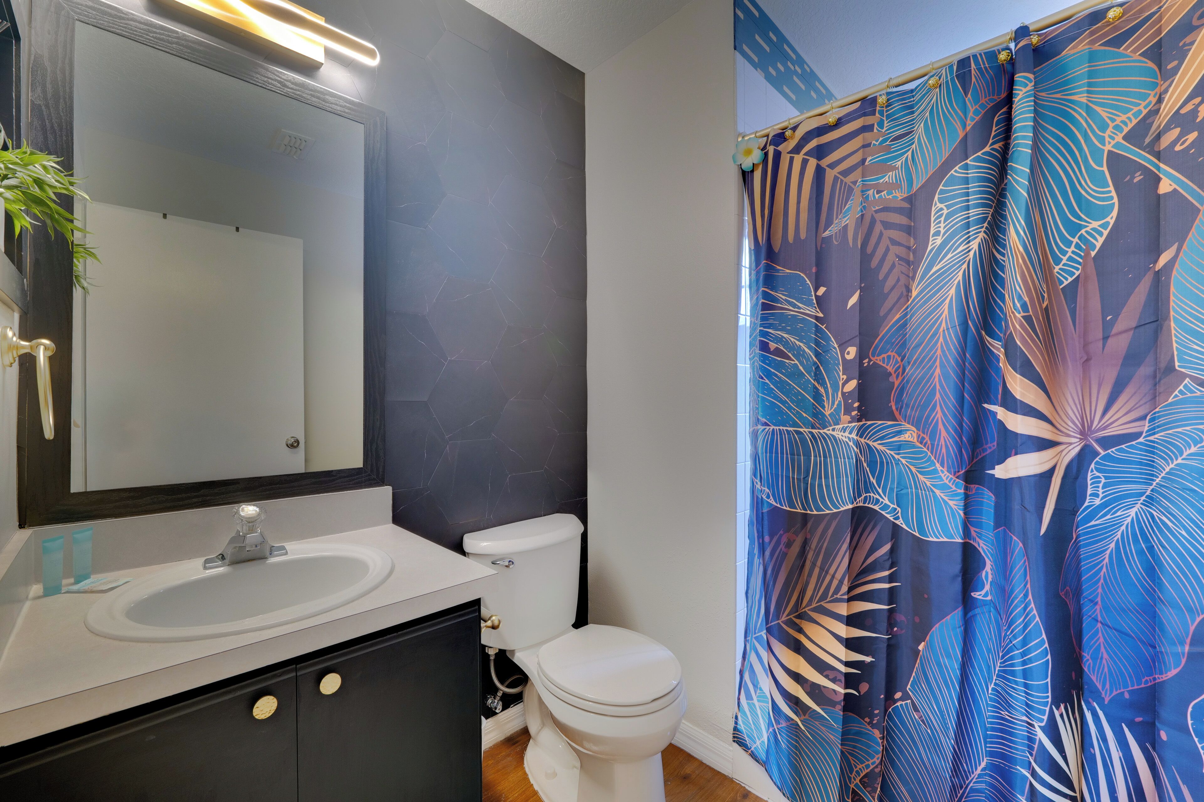 A bathroom with a white sink, a toilet, and a shower curtain with a tropical leaf pattern.