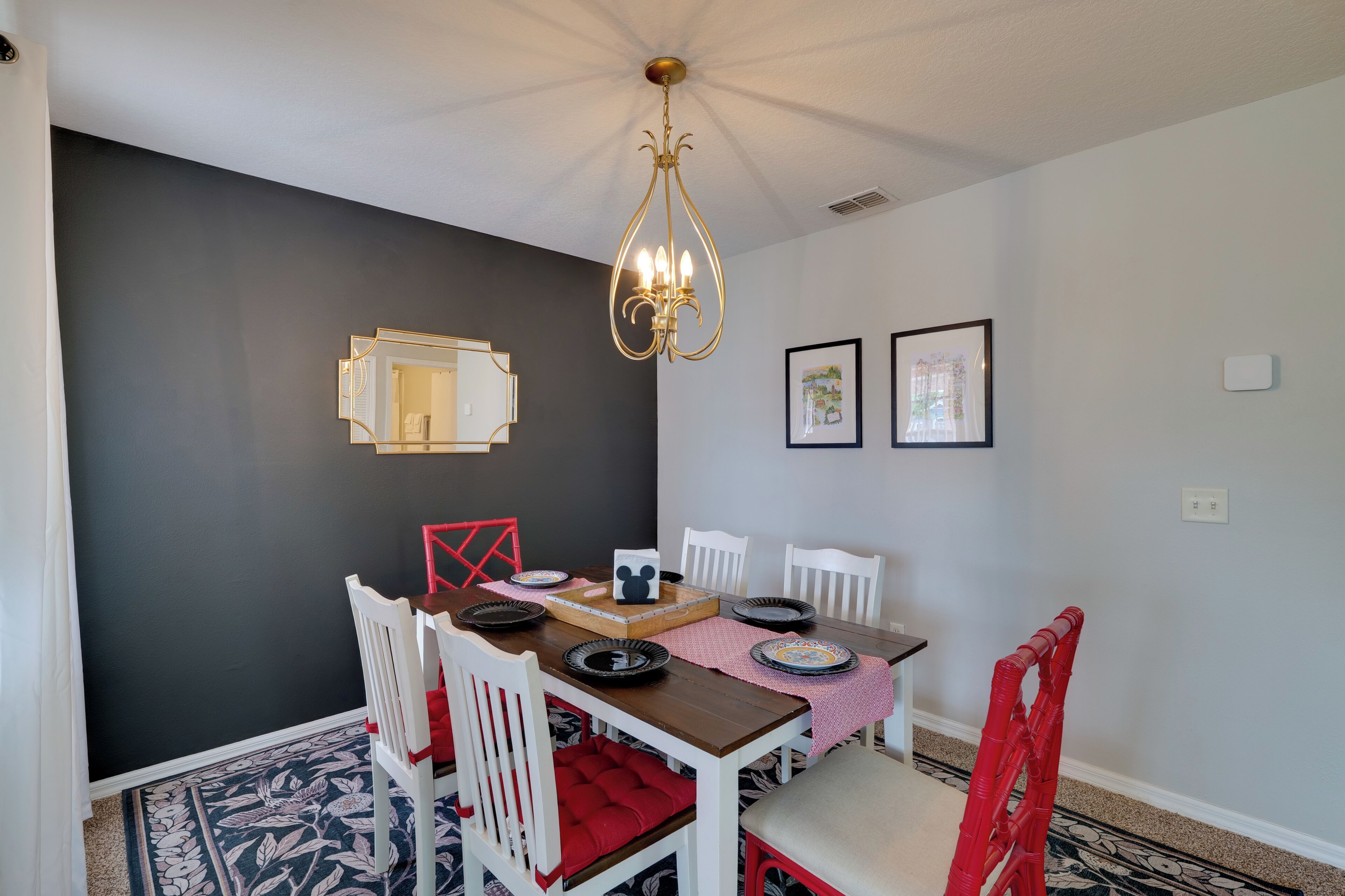 A dining area with a dark wall, a chandelier, framed pictures, and a Mickey Mouse-themed centerpiece.