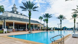 Ein Swimmingpool mit überdachter Liegefläche, Palmen und einem Gebäude mit einem Turm.