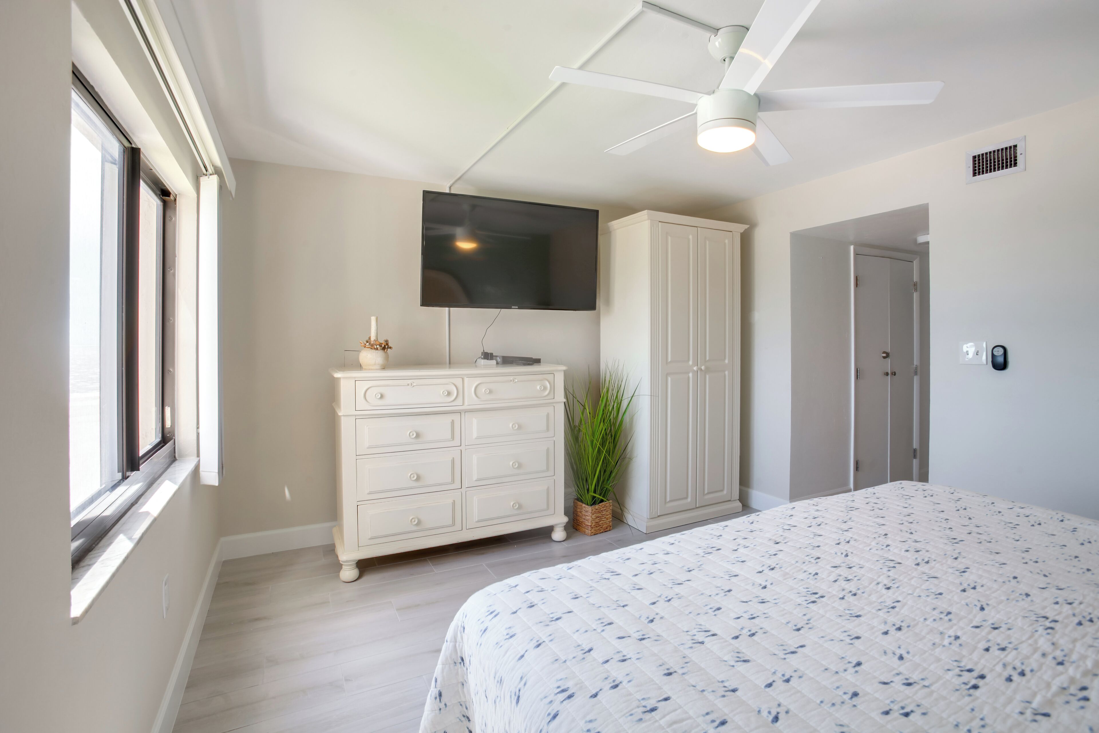 A bedroom with a bed, a dresser, a television, a ceiling fan, and a door.