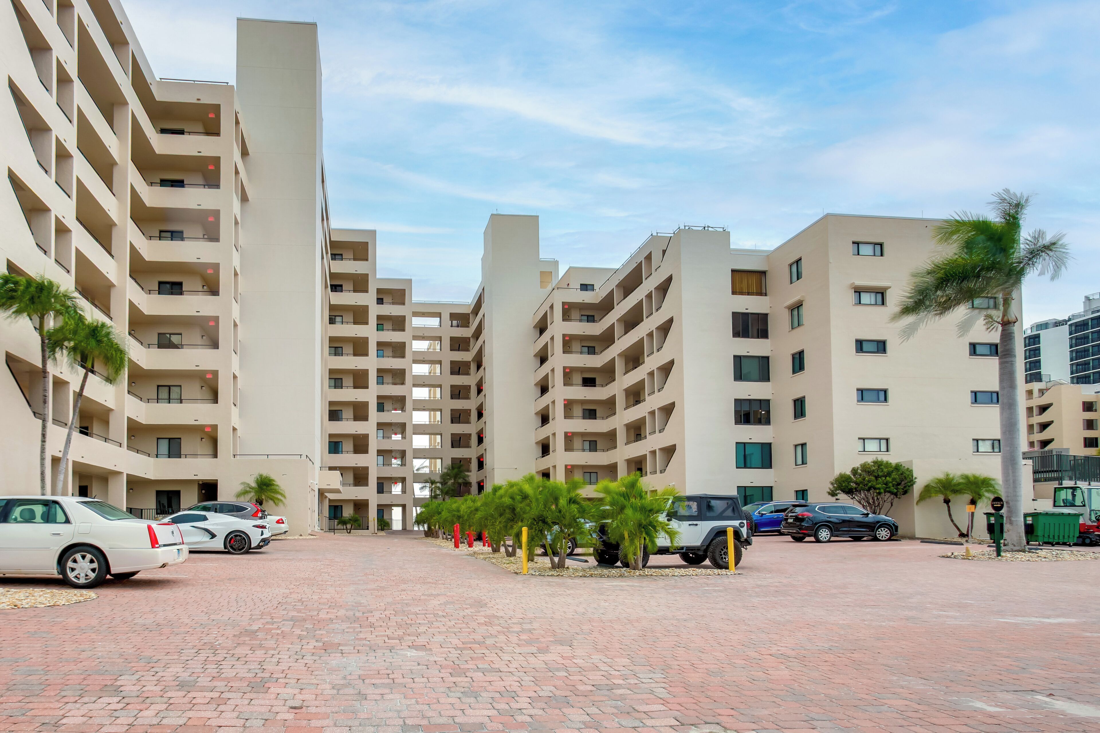 A modern apartment complex with multiple floors, a paved courtyard, and parked cars.
