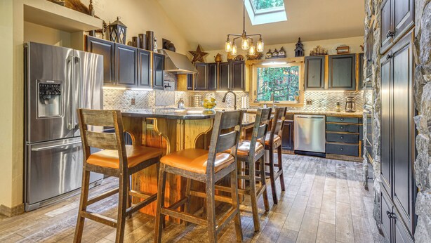 Une cuisine avec un mur en pierre, des poutres en bois au plafond, une verrière, des appareils électroménagers en acier inoxydable et un coin bar avec des chaises en bois.