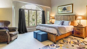 Une chambre à coucher avec un grand lit, une table de chevet en bois, une chaise et une fenêtre avec des rideaux.
