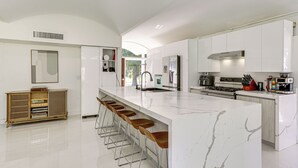 A modern kitchen with a large island, bar stools, white cabinetry, and stainless steel appliances. - 2 Mi to Fsu: Unique Home w/ Patio & Spacious Yard (Tallahassee)