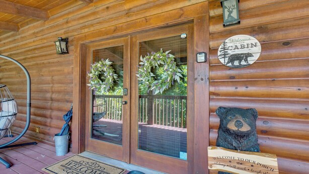 Entrada a una cabaña de madera con un letrero de bienvenida, una decoración de oso y un cartel con el número de la cabaña.